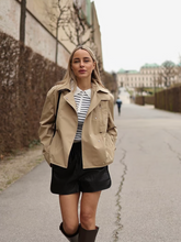a lady wears a sweater with crop trench coat with black shorts and boots